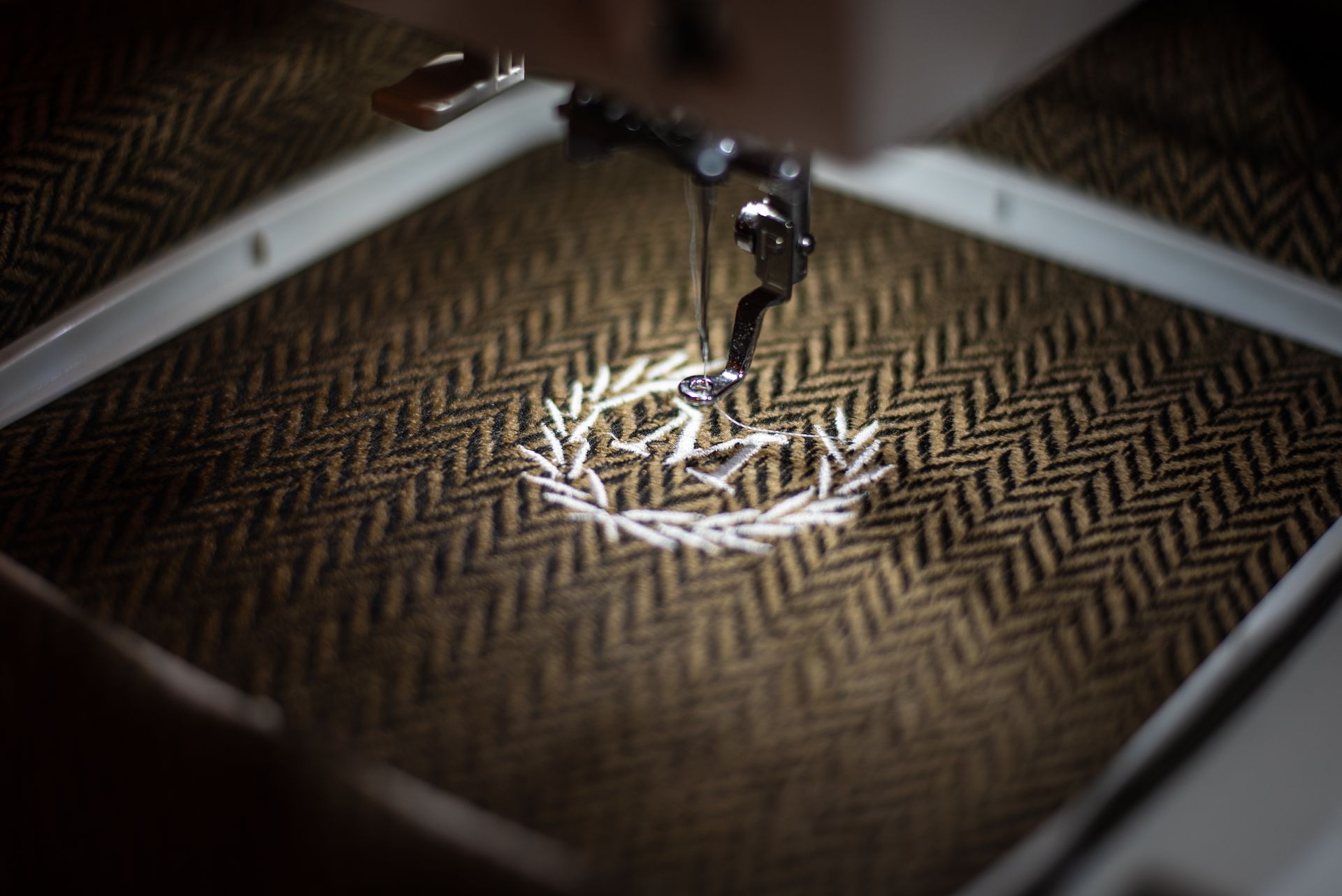 Close-up of an industrial sewing machine stitching a circular zigzag pattern on textured fabric.