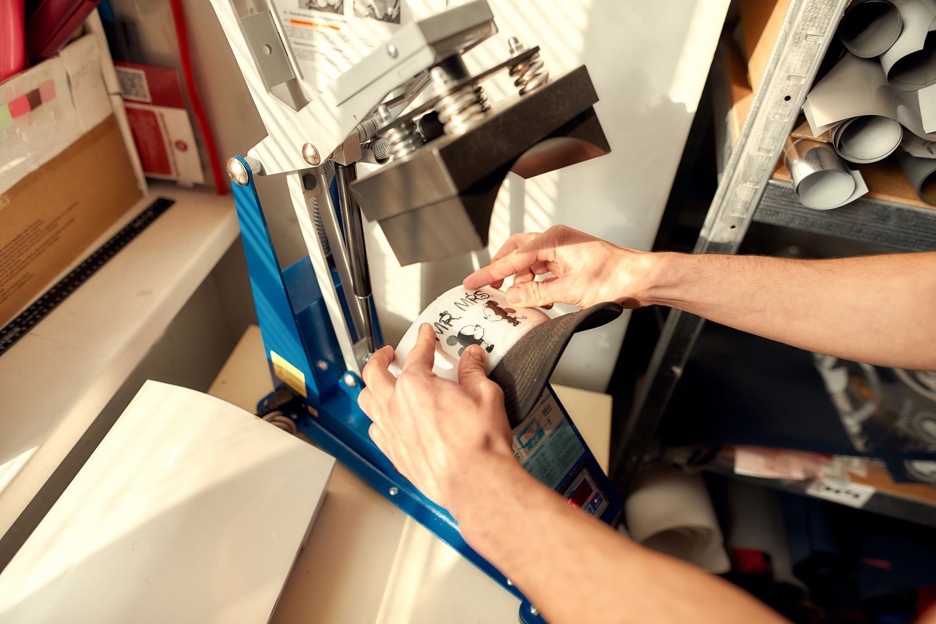 Hands using a blue machine to wrap or print labels in a cluttered workshop area