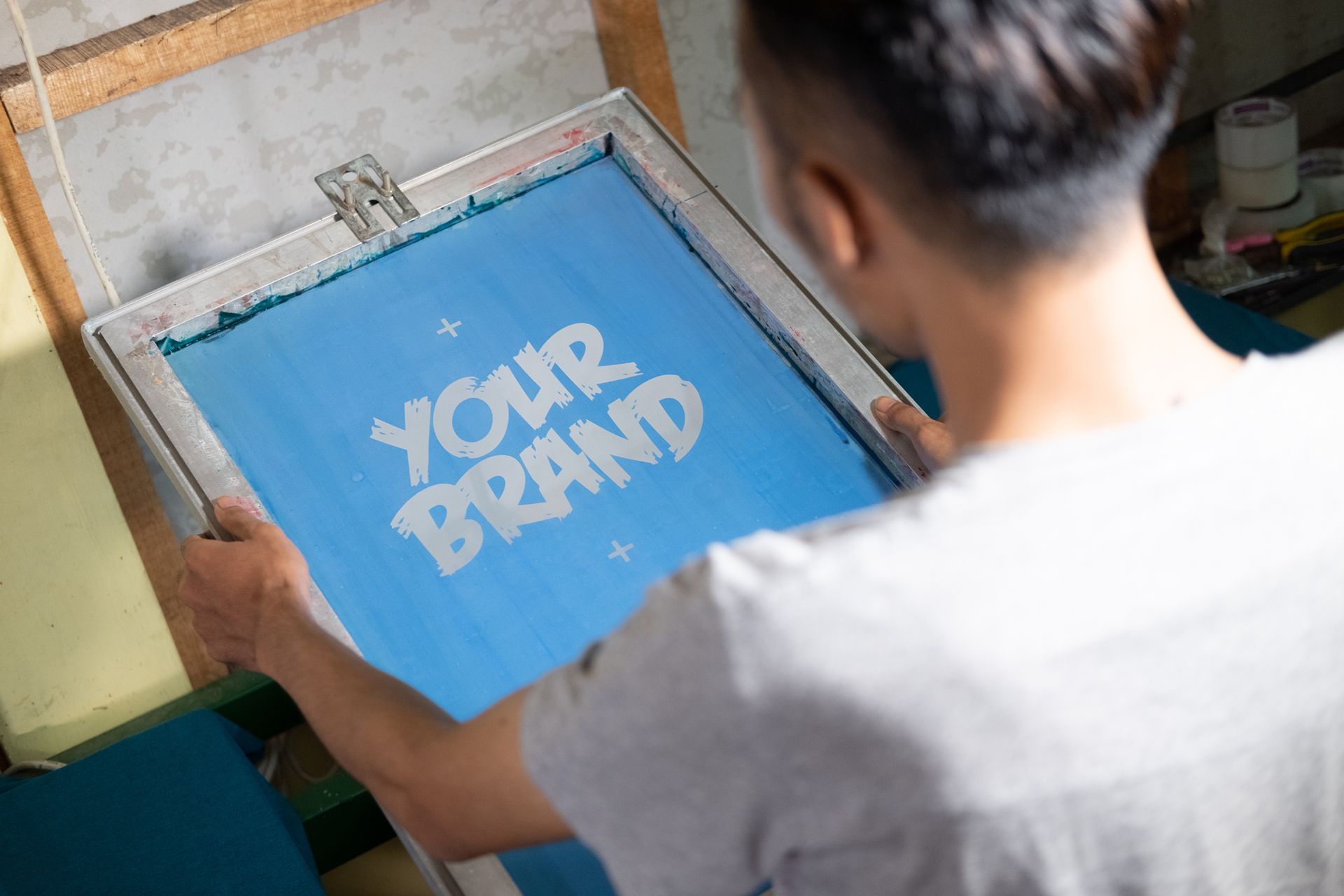 Person printing a blue “YOUR BRAND” design on a screen-printing frame