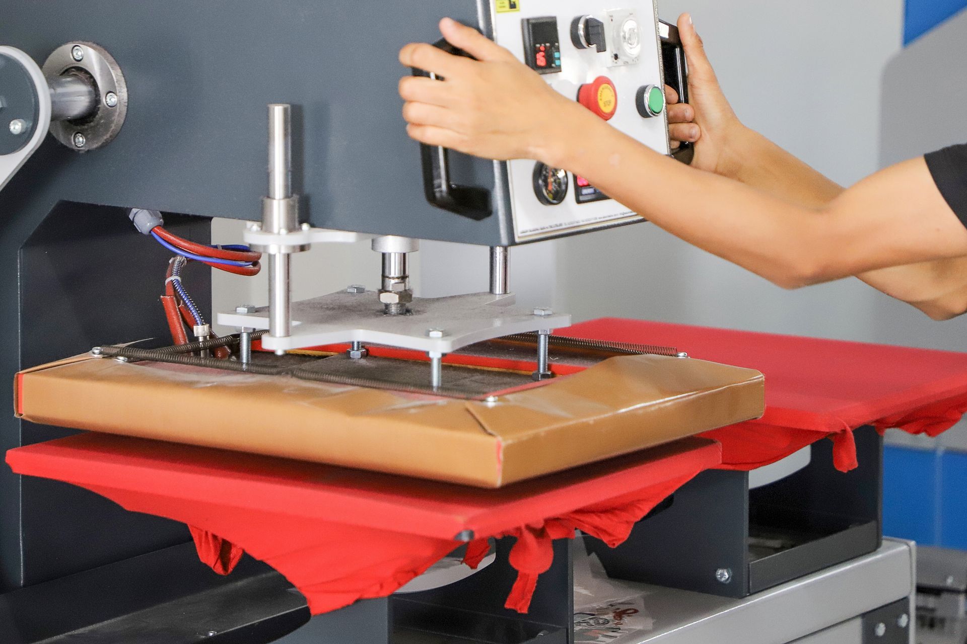 Person operating a heat press to print on a red fabric item on a worktable