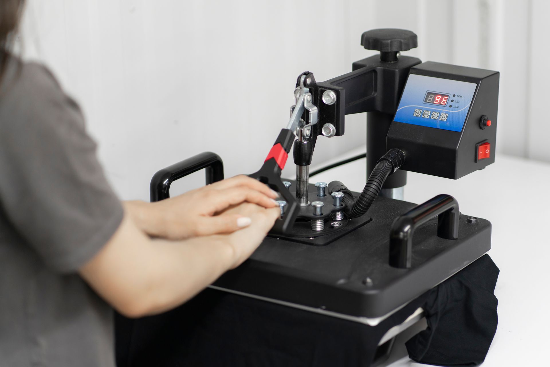 Hands operating a black desktop machine with a small screen and controls in a bright room