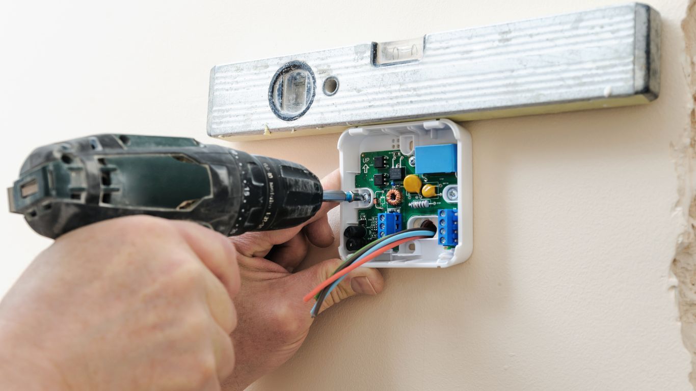 TSC-HVAC - A person is installing a thermostat on a wall with a drill.