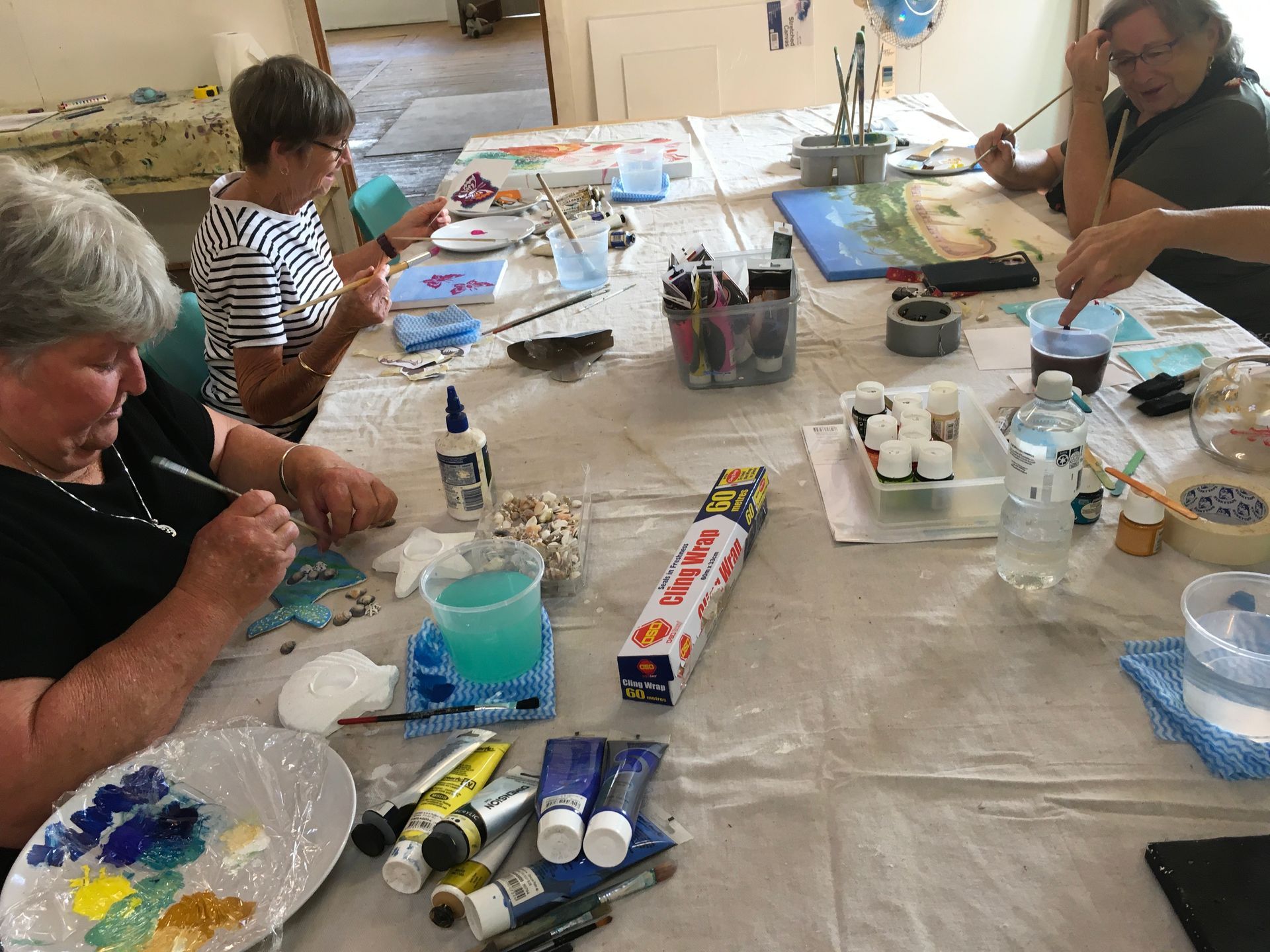 A group of people are sitting at a table painting.