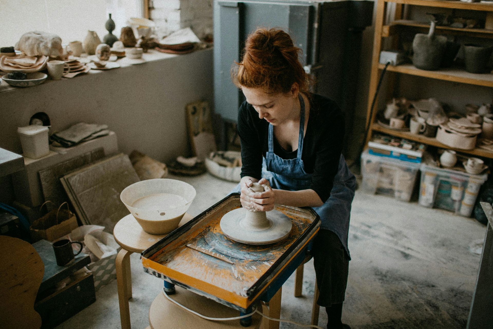 A woman is sitting at a pottery wheel making a pot.