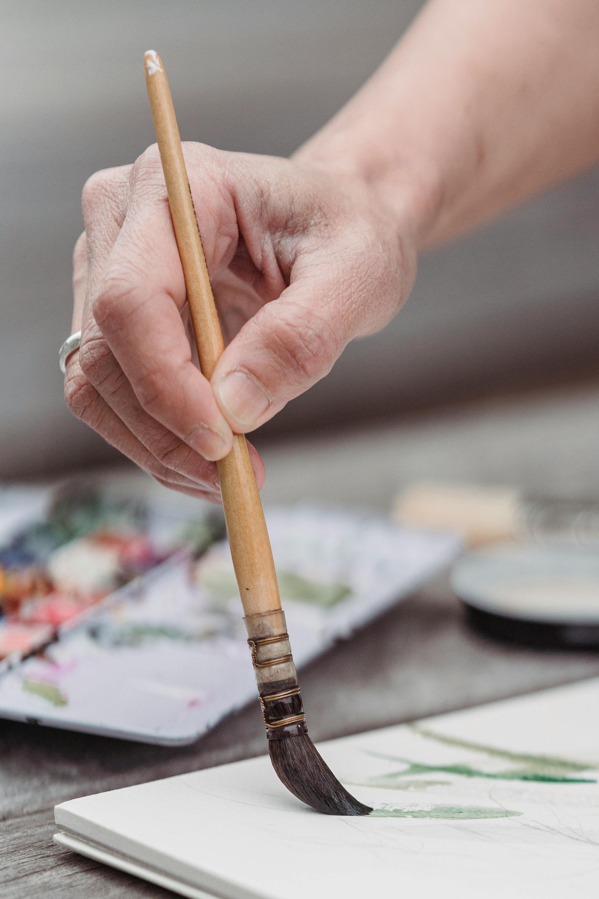 A person is holding a brush and painting on a piece of paper.
