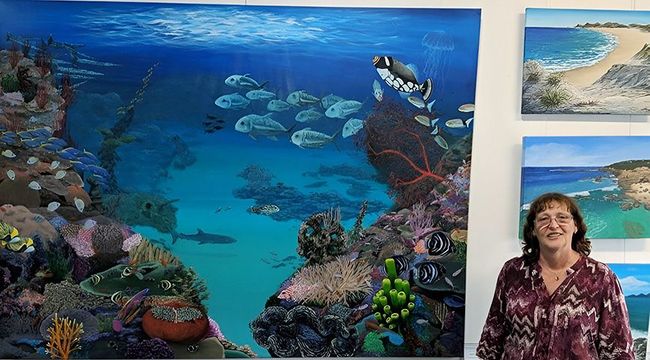 A woman is standing in front of a painting of a coral reef.