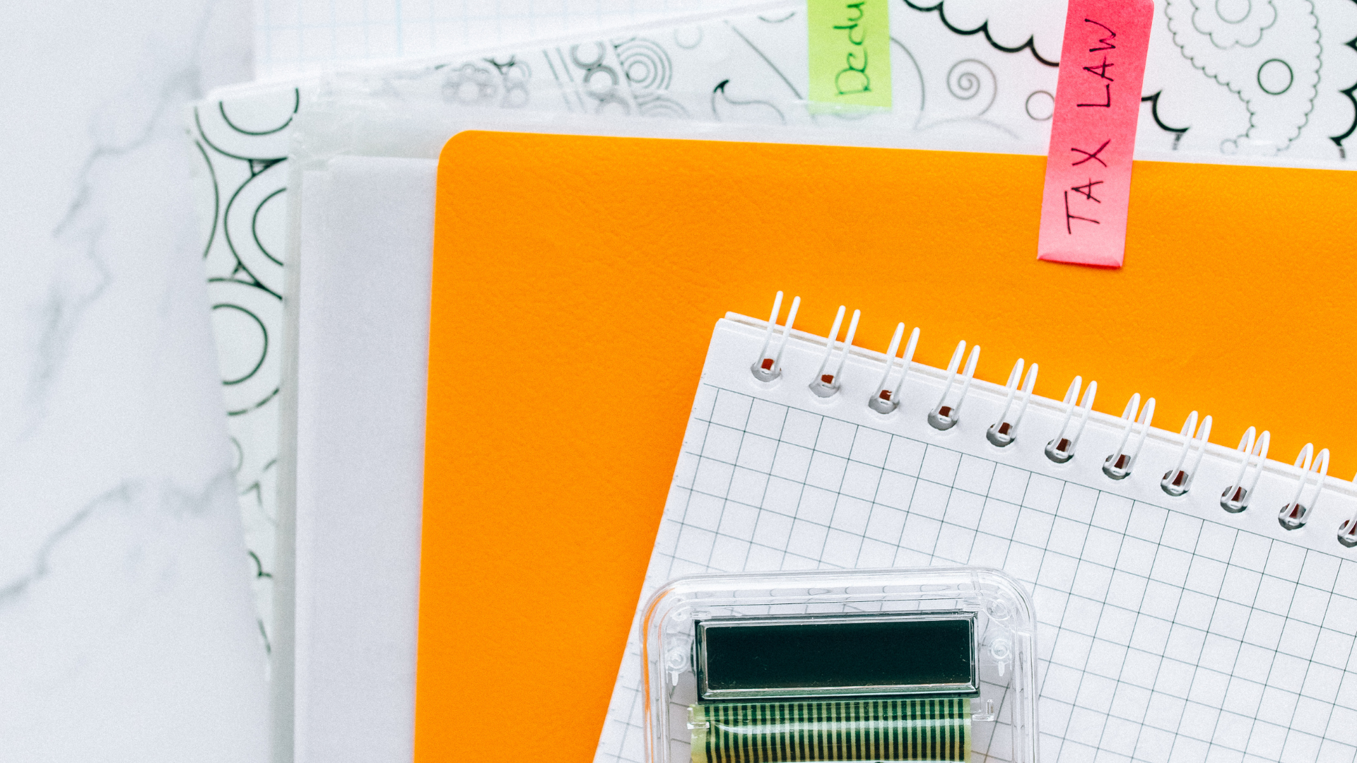 Notebooks and other stationary on a marble surface, including an orange book with a