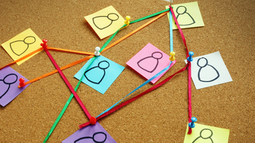 Corkboard with sticky notes of people connected by string, representing relationships.