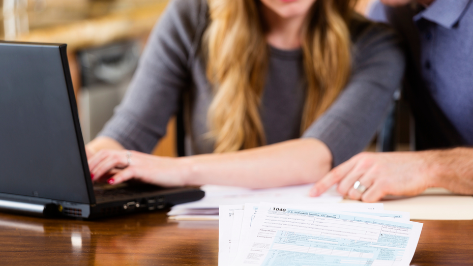 Couple reviewing tax documents and laptop, one pointing at paper, indoor setting.