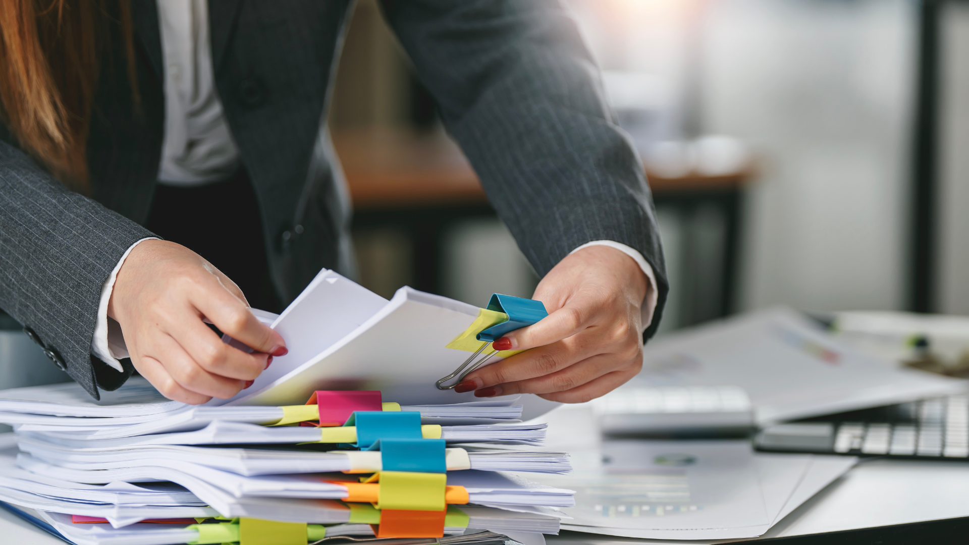 Woman in a suit sorting paperwork, using binder clips in an office setting.