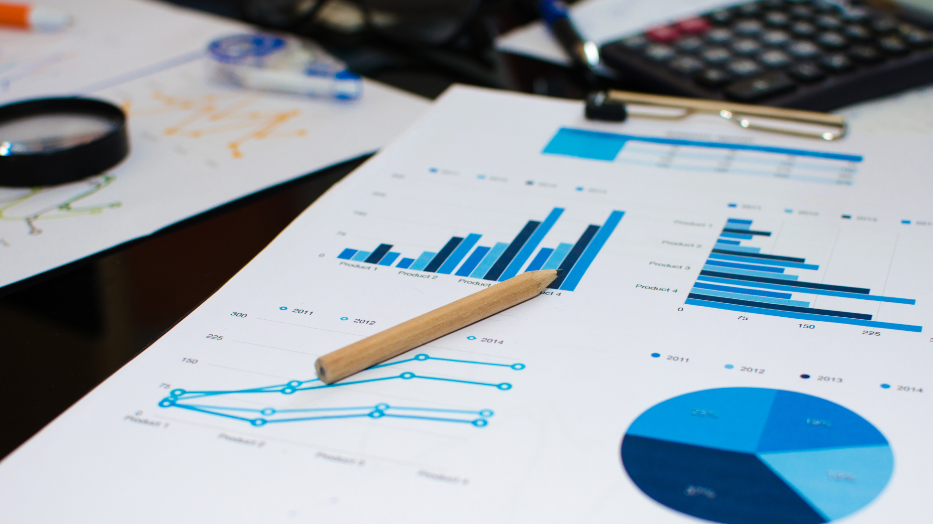Graphs and charts with pencil, calculator, and magnifying glass on desk, analyzing data.