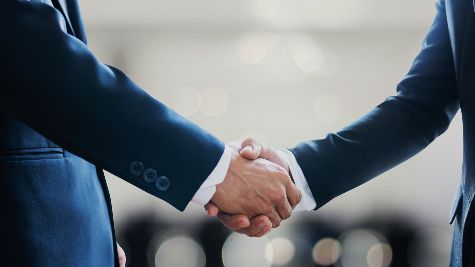 Two people in suits shake hands, a sign of agreement or partnership.