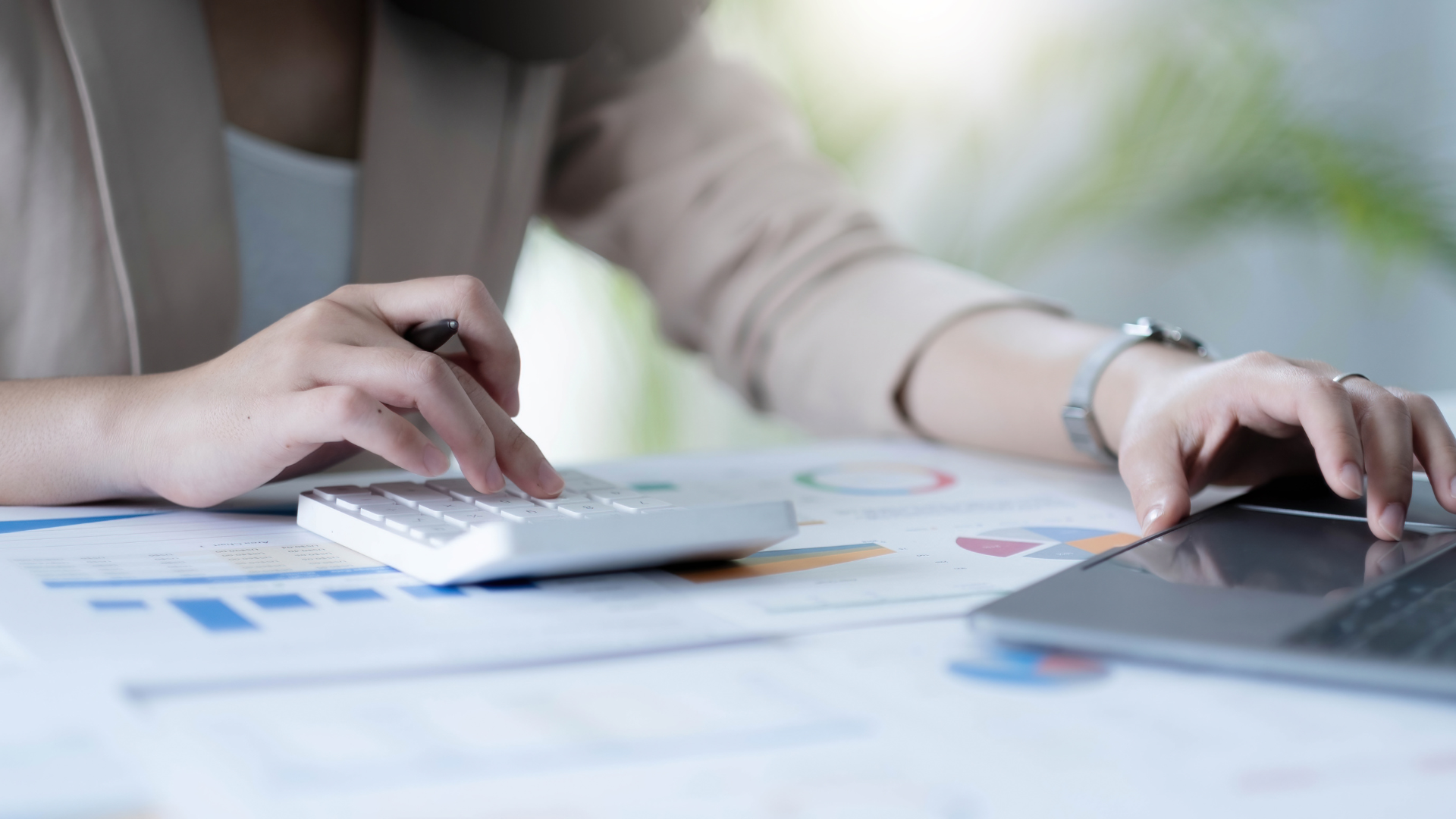 Woman using a calculator and laptop, reviewing financial documents at a desk.