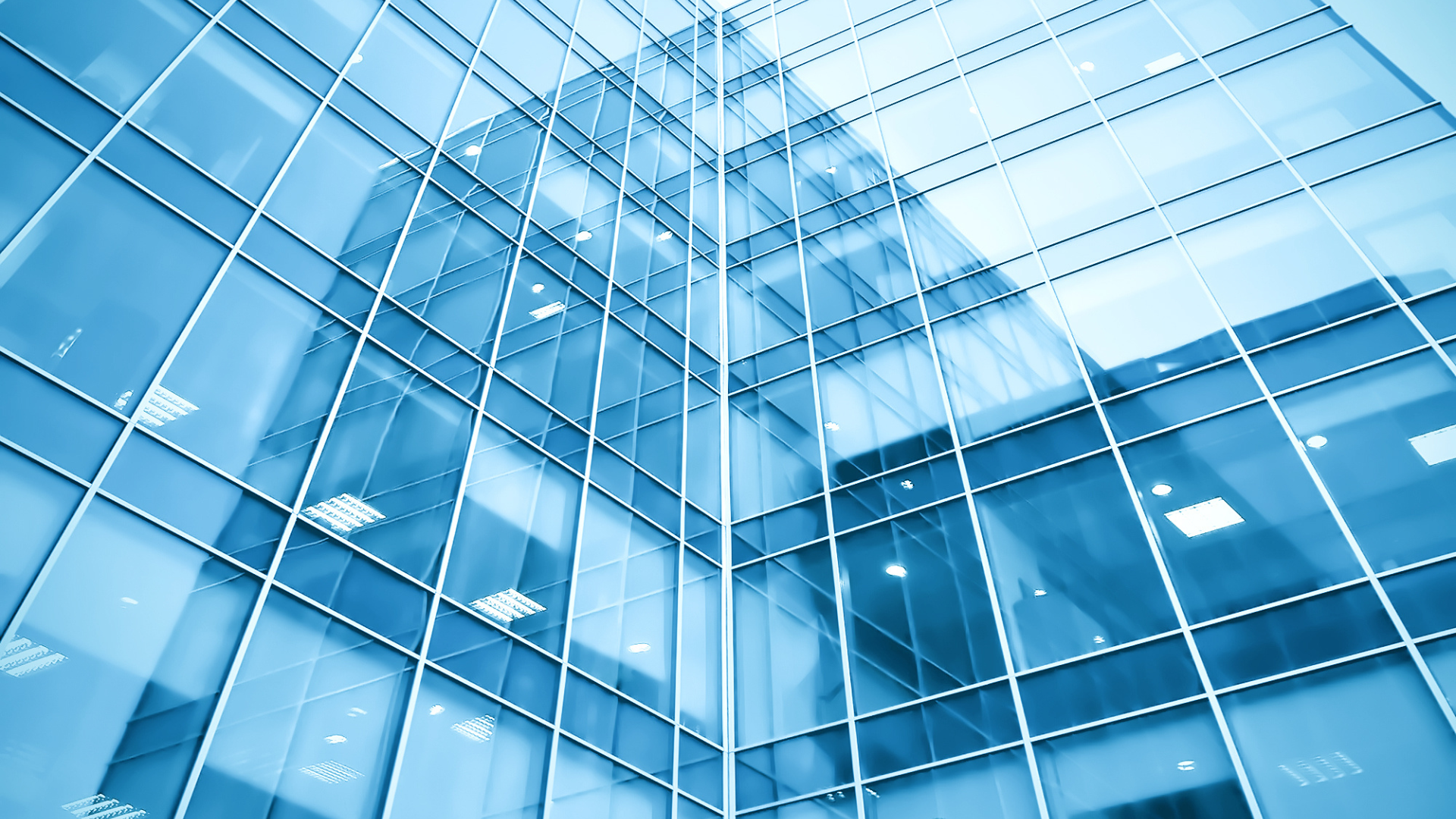Modern glass skyscraper, blue-tinted, reflecting the sky, with a low-angle perspective.