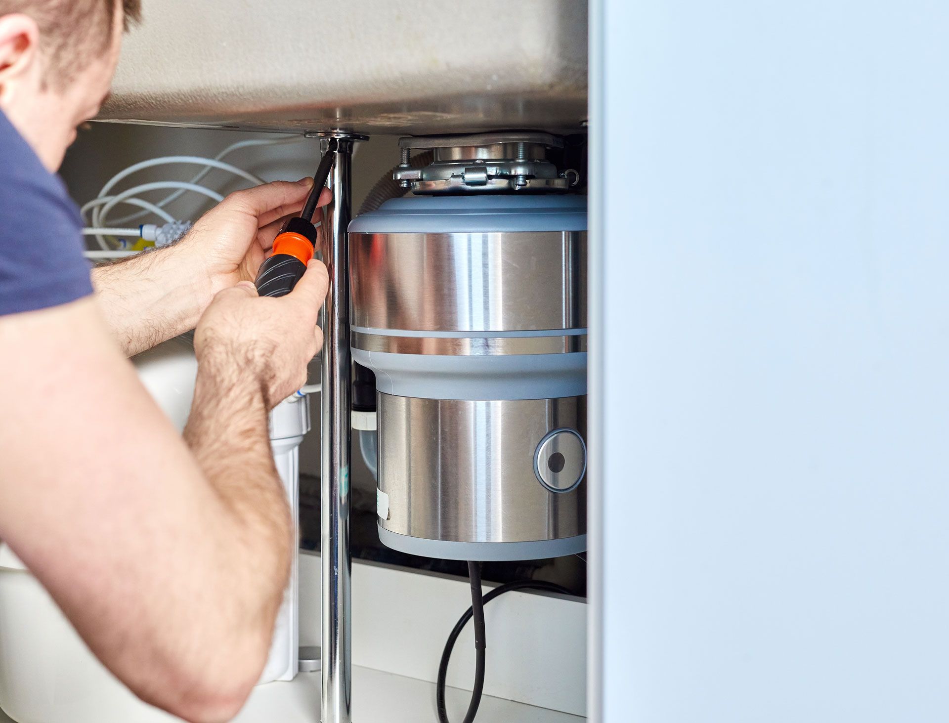 A man is fixing a garbage disposal under a sink.