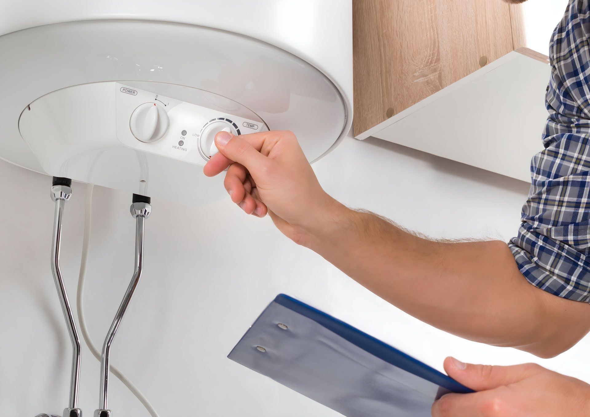 A man is adjusting the temperature of a water heater while holding a clipboard.
