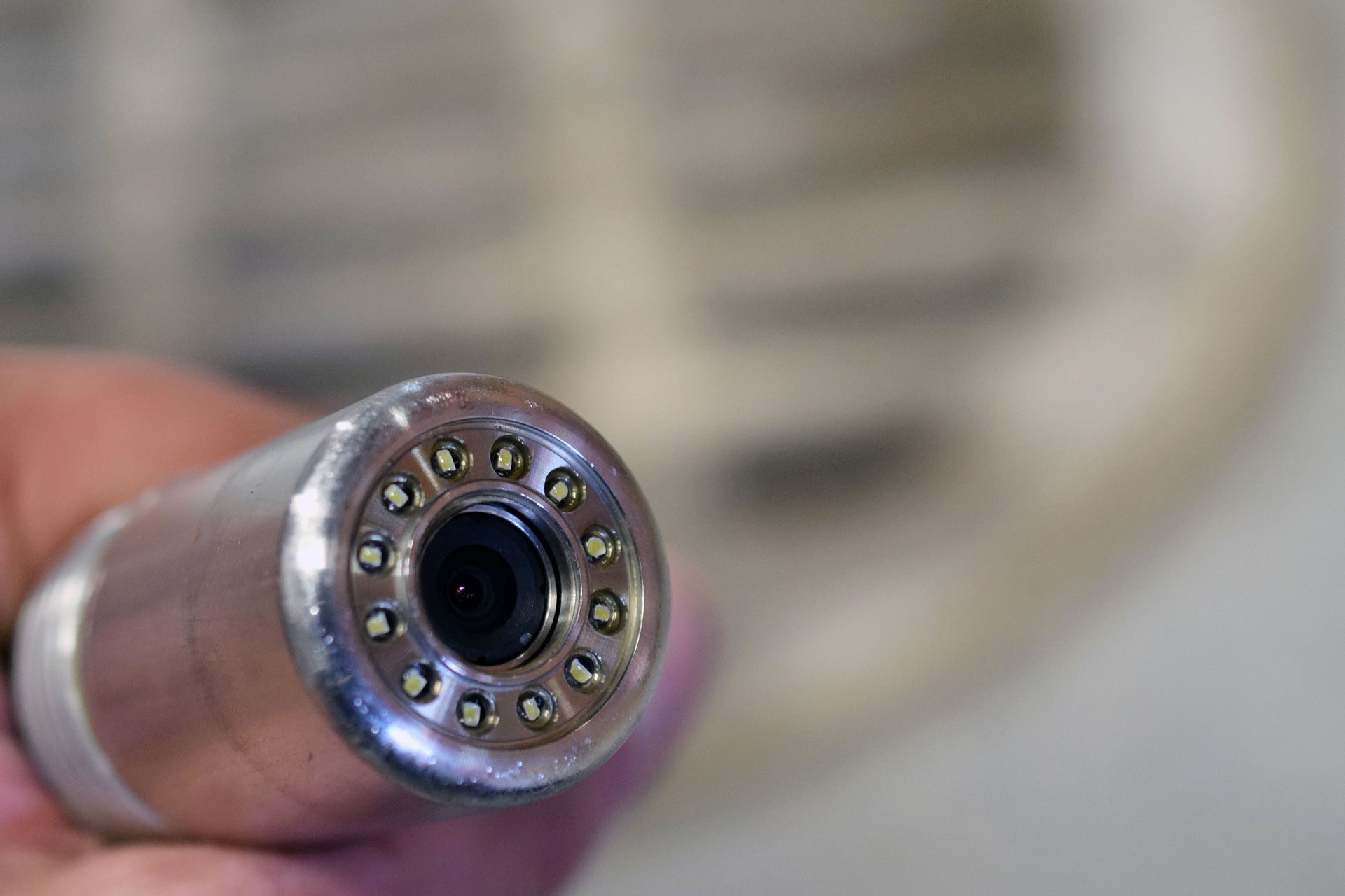 Close-up of a cylindrical camera endoscope with a lens and surrounding small lights, held in a hand.