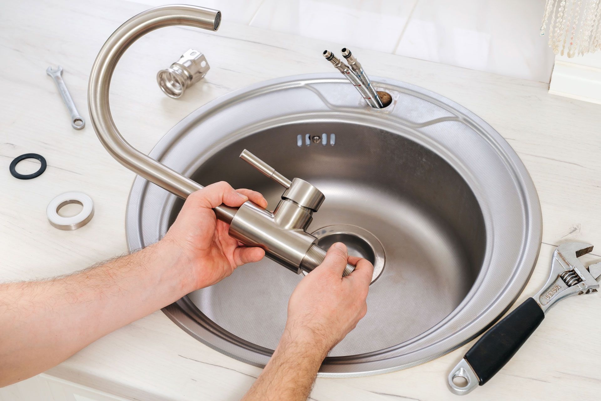 Hands assembling a new kitchen faucet over a stainless steel sink, with tools and parts visible.