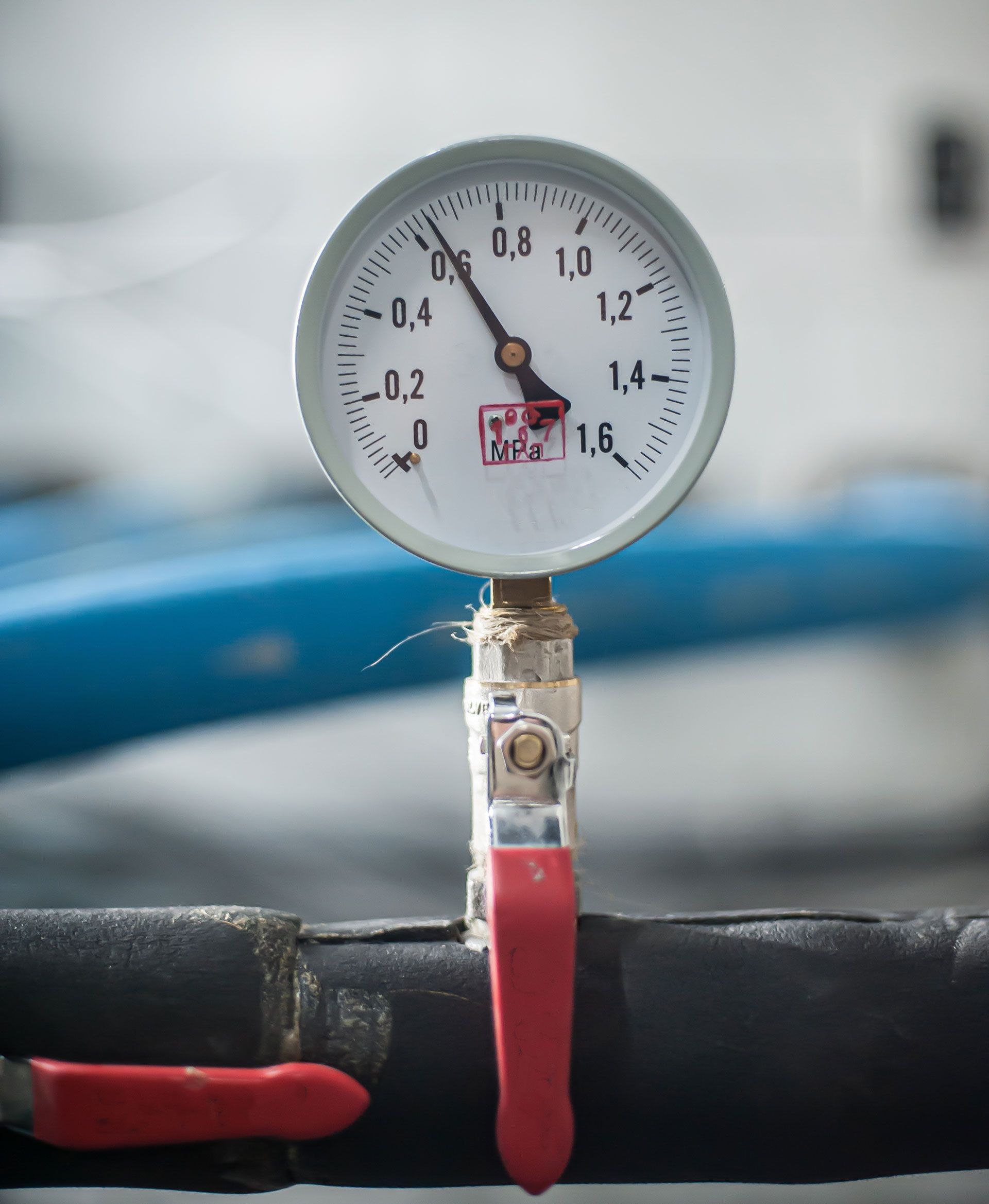 Pressure gauge with a white face, showing a reading near 0.6, connected to black pipes with red valve handles.