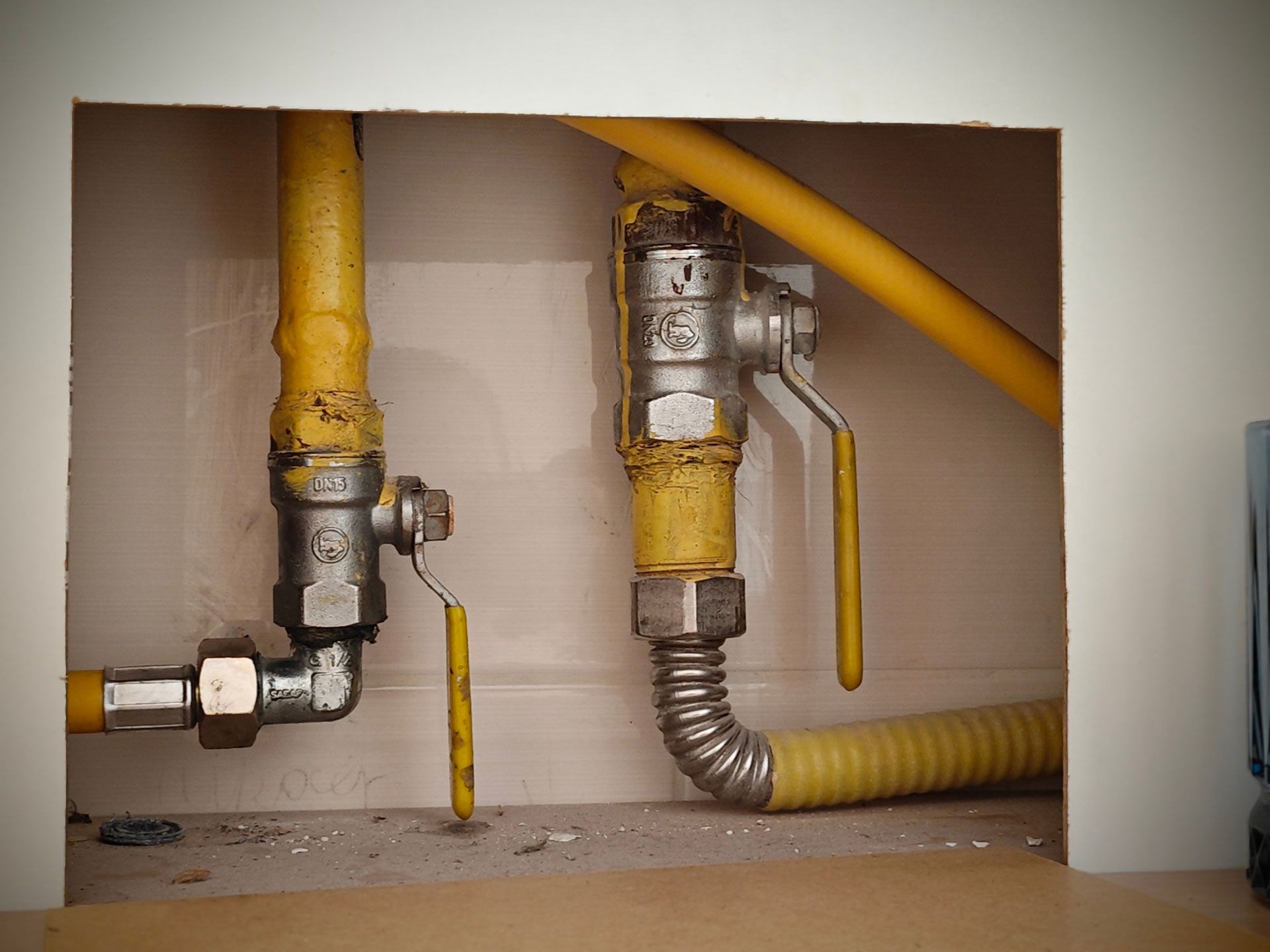 Gas pipes and shut-off valves in a recessed white wall. Yellow pipes with silver fittings and two yellow-handled valves.