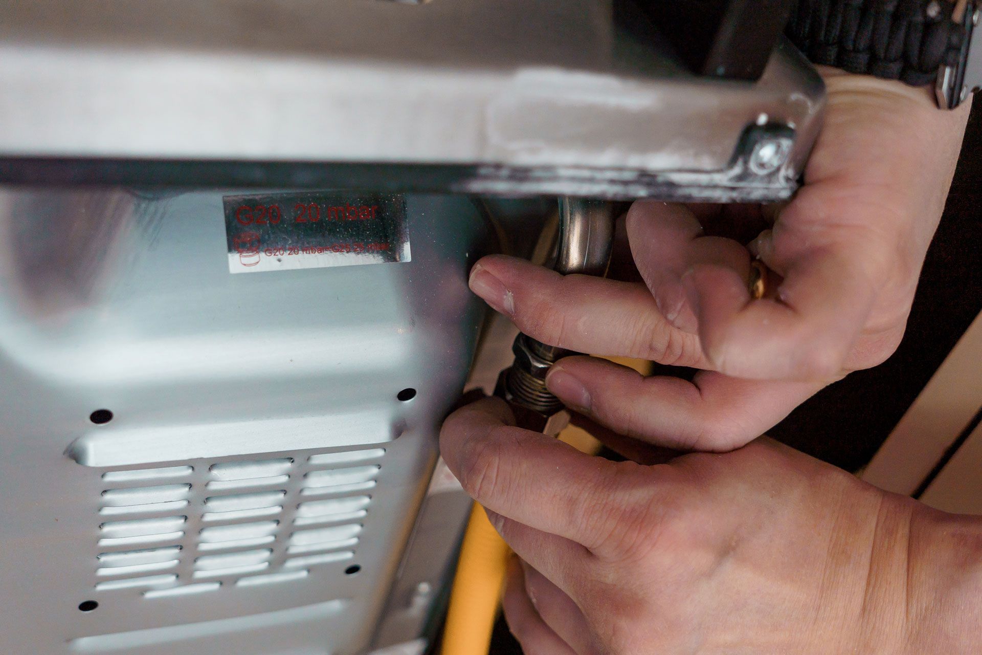 Hands connecting a yellow gas line to a metal appliance.