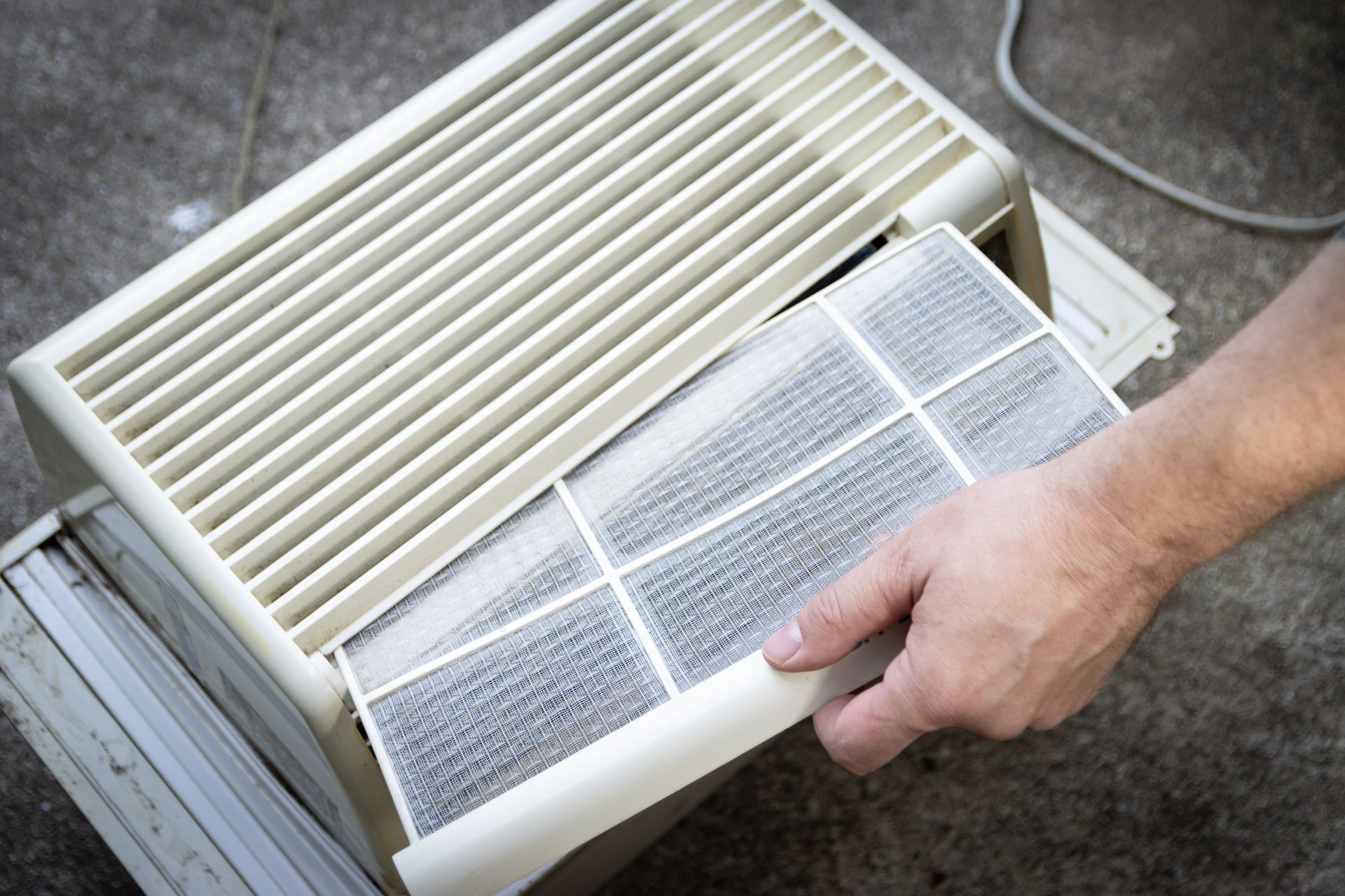 Hand removing a dirty air filter from a beige air purifier.