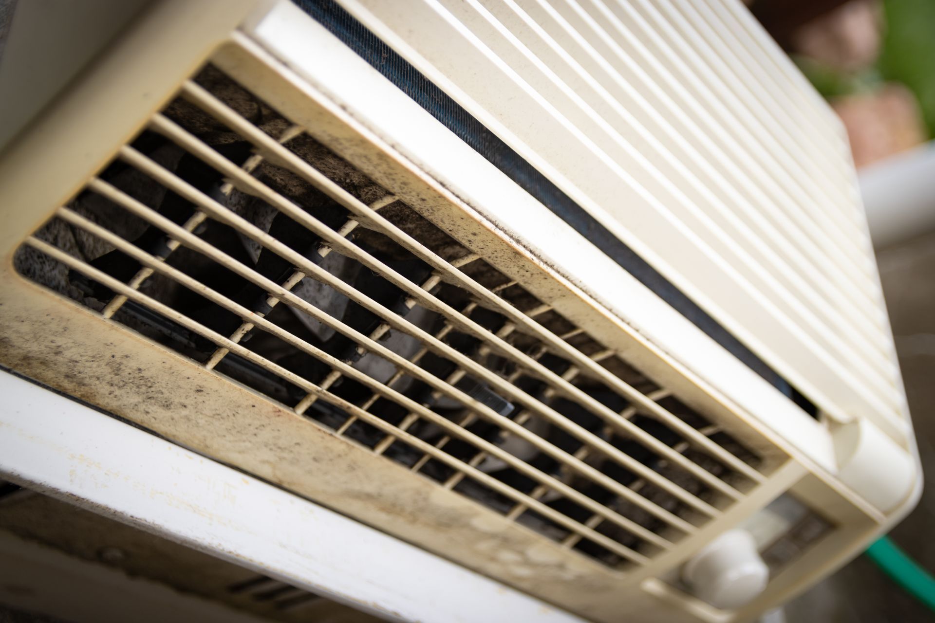 Dirty, off-white air conditioner unit, close-up, with vents covered in dust and debris.