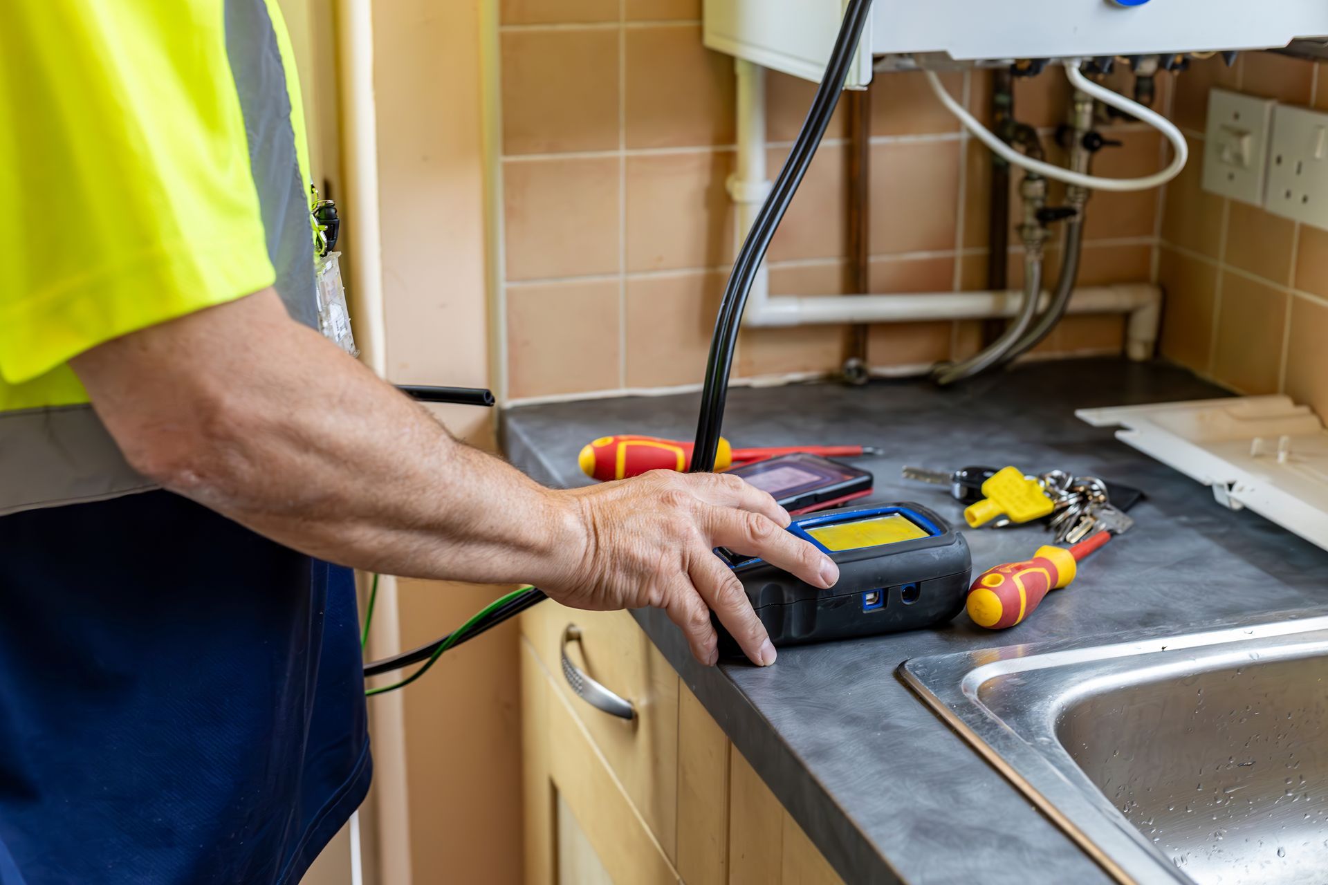 Plumber in yellow safety vest tests a gas appliance in a kitchen; tools and sink visible.