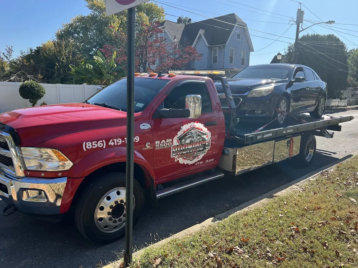 Red tow truck with a car on its bed, parked on the side of a street.