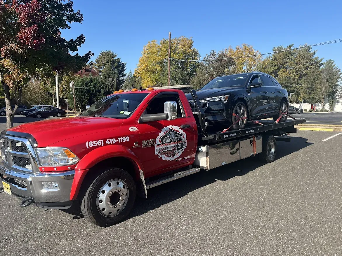 Red tow truck carrying a black car on a sunny day in a parking lot.