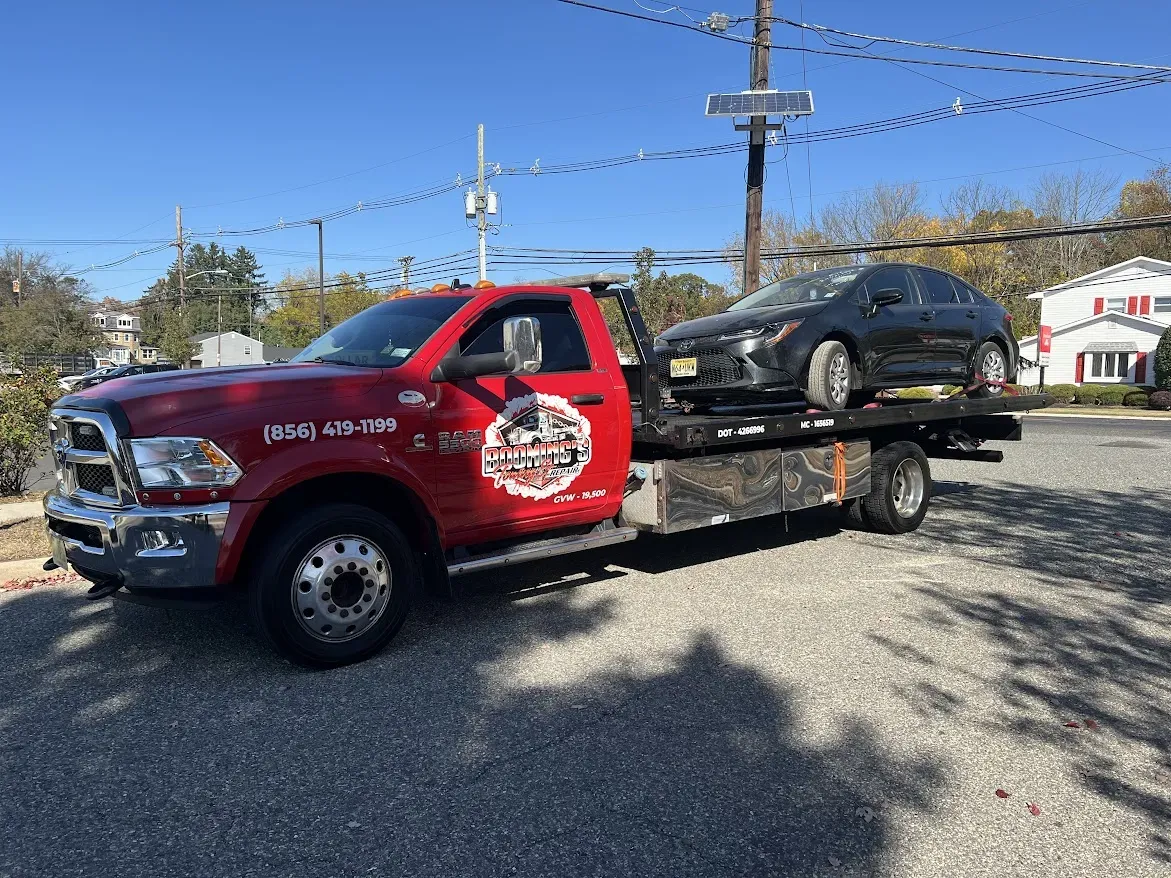 Red tow truck carrying a black car on a sunny day.