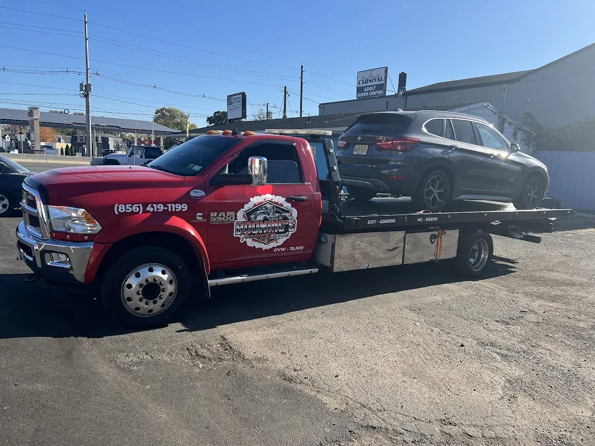 Red tow truck carrying a black car on a sunny day, parked in front of a building.