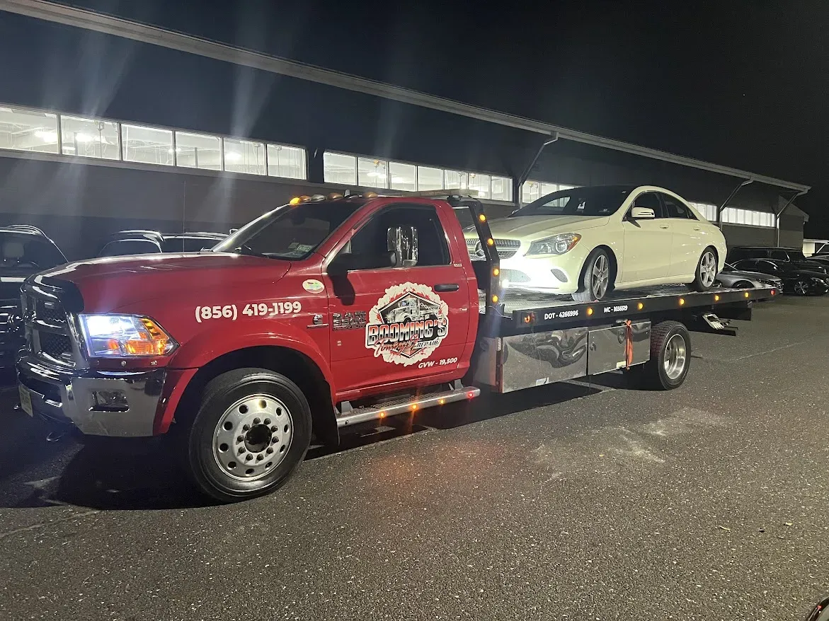 Red tow truck carrying a white car on a flatbed at night.