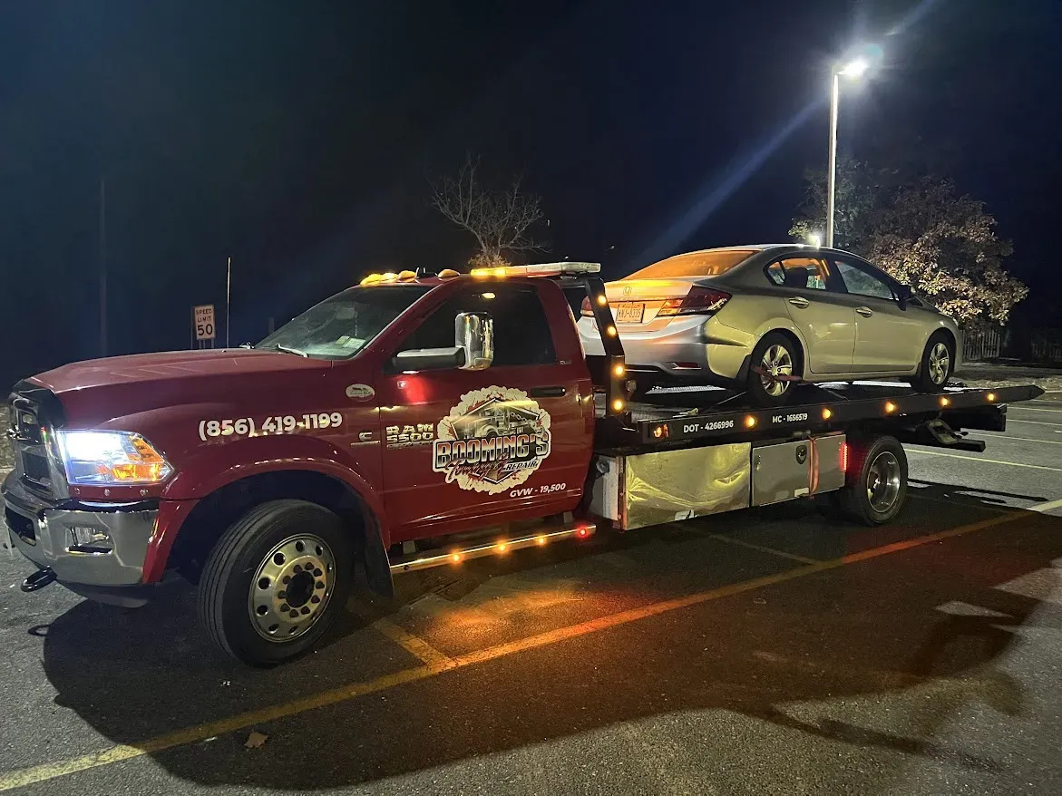 A red tow truck hauling a silver car at night in a parking lot.