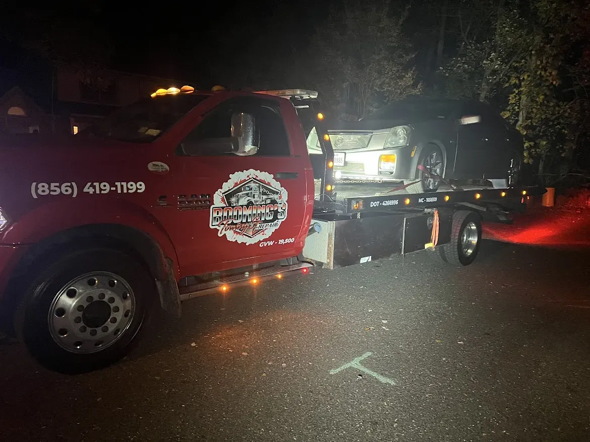 Red tow truck at night loading a car. Street, emergency lights, and a faded marking visible.
