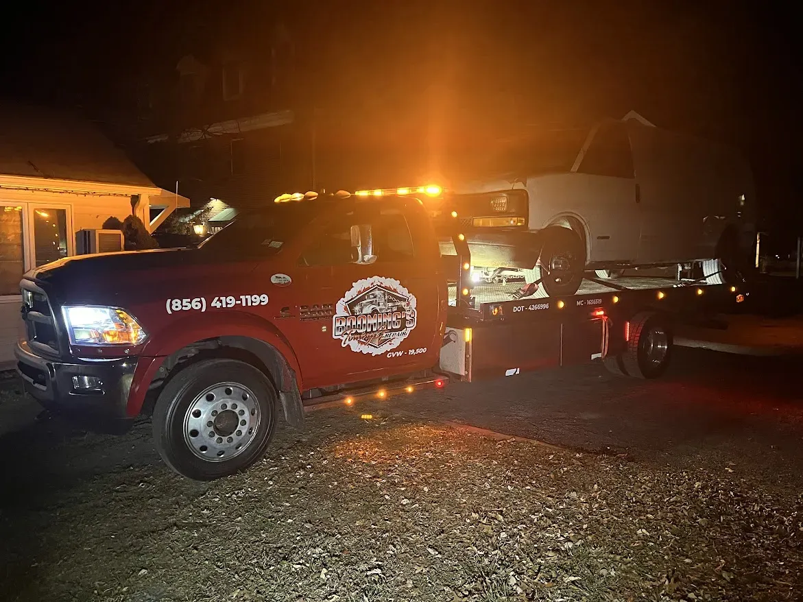 Red tow truck with flashing lights towing a trailer at night.