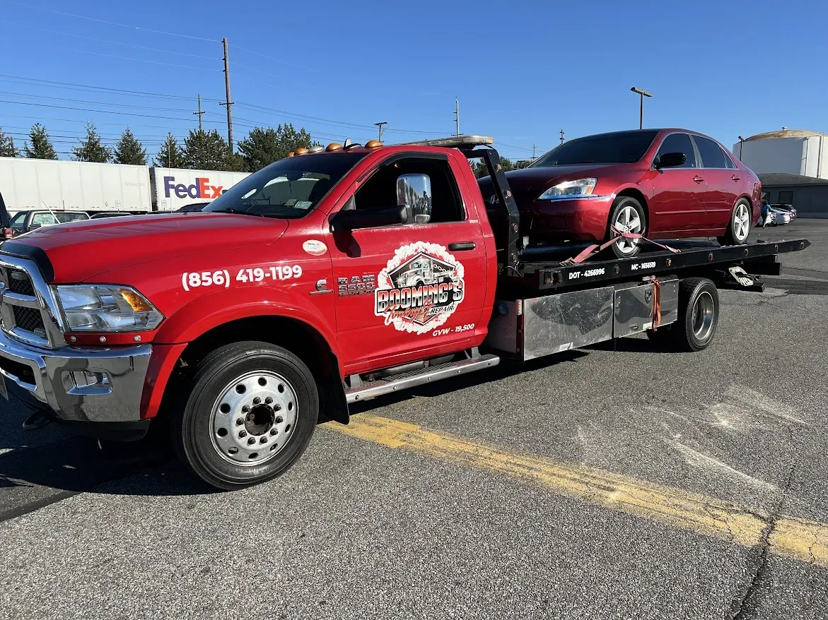 Red tow truck hauling a red car in a parking lot.