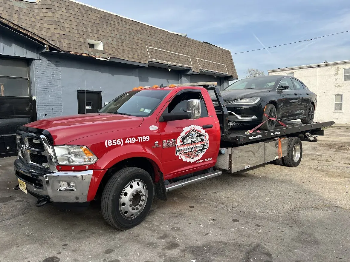 Red tow truck carrying a black car, parked outside a building.