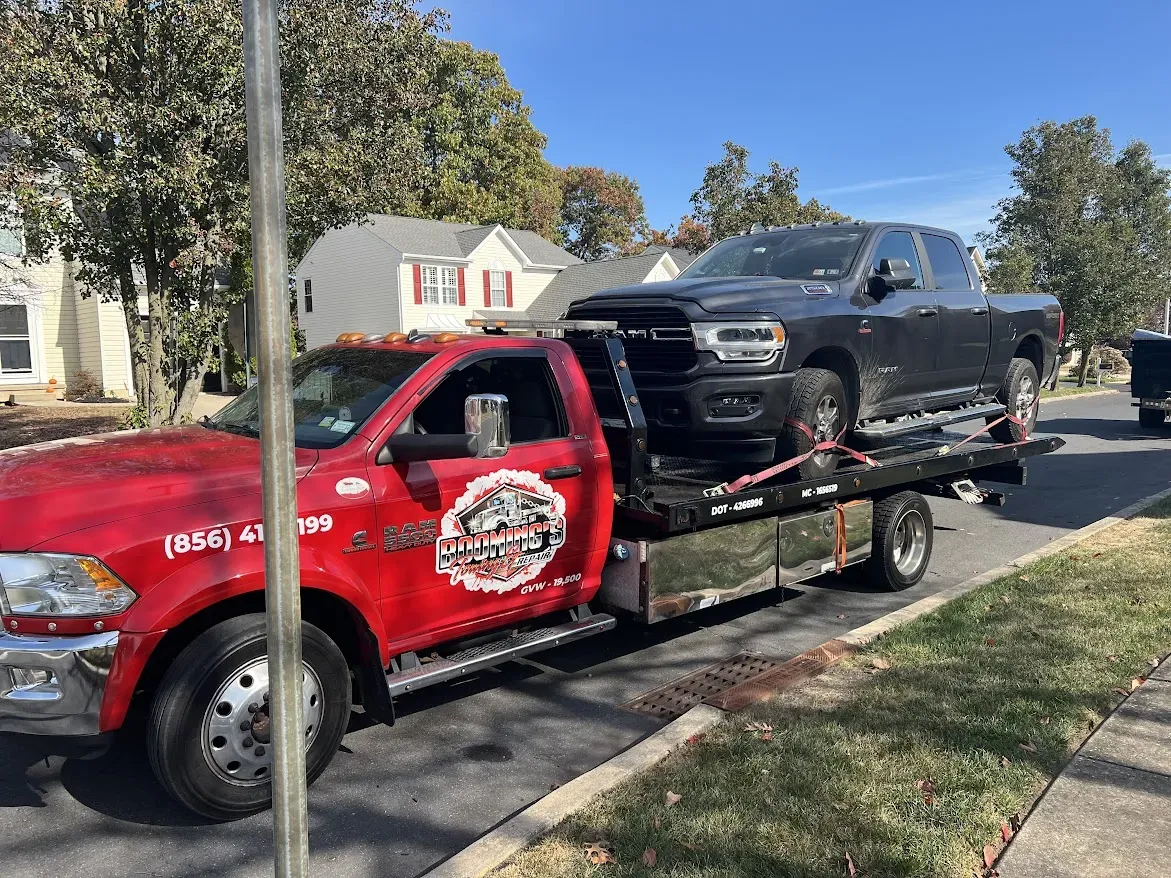 Red tow truck carrying a black pickup truck on a residential street.