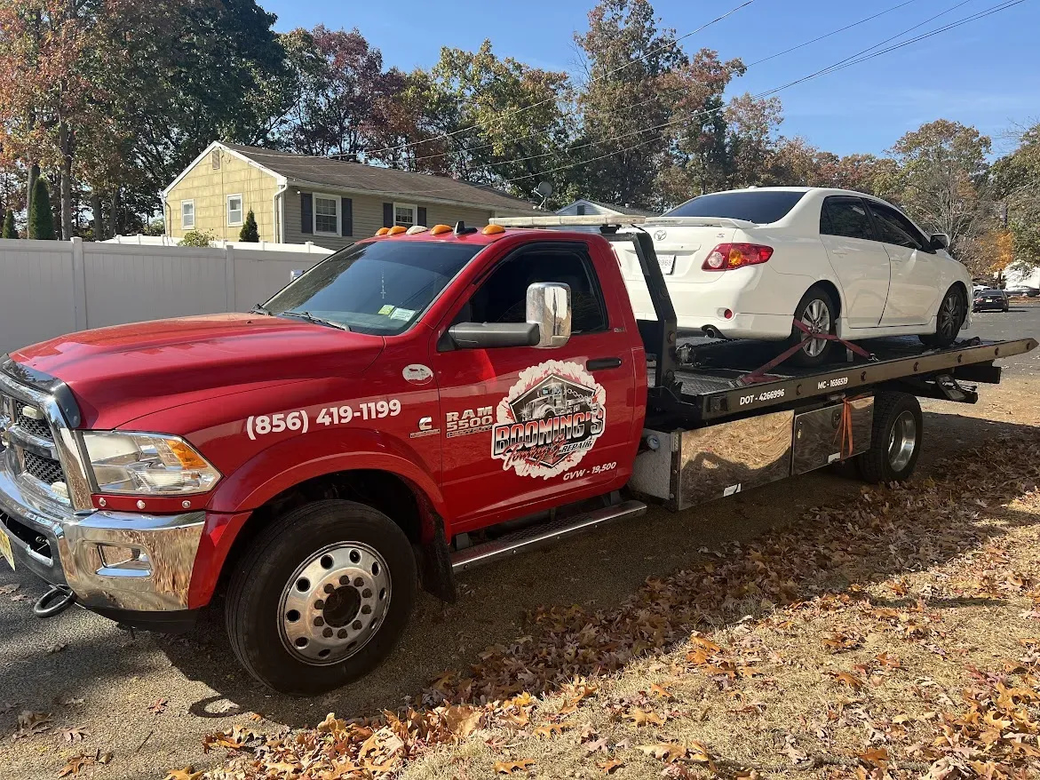 Red tow truck hauling a white sedan on a sunny day.