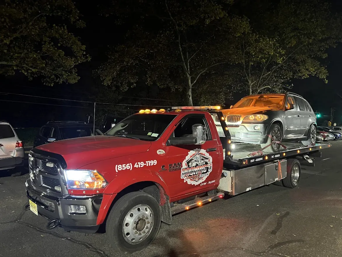 Tow truck with a damaged silver SUV on a road at night.