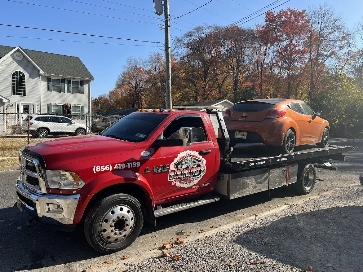Red tow truck carrying an orange car on a sunny day.
