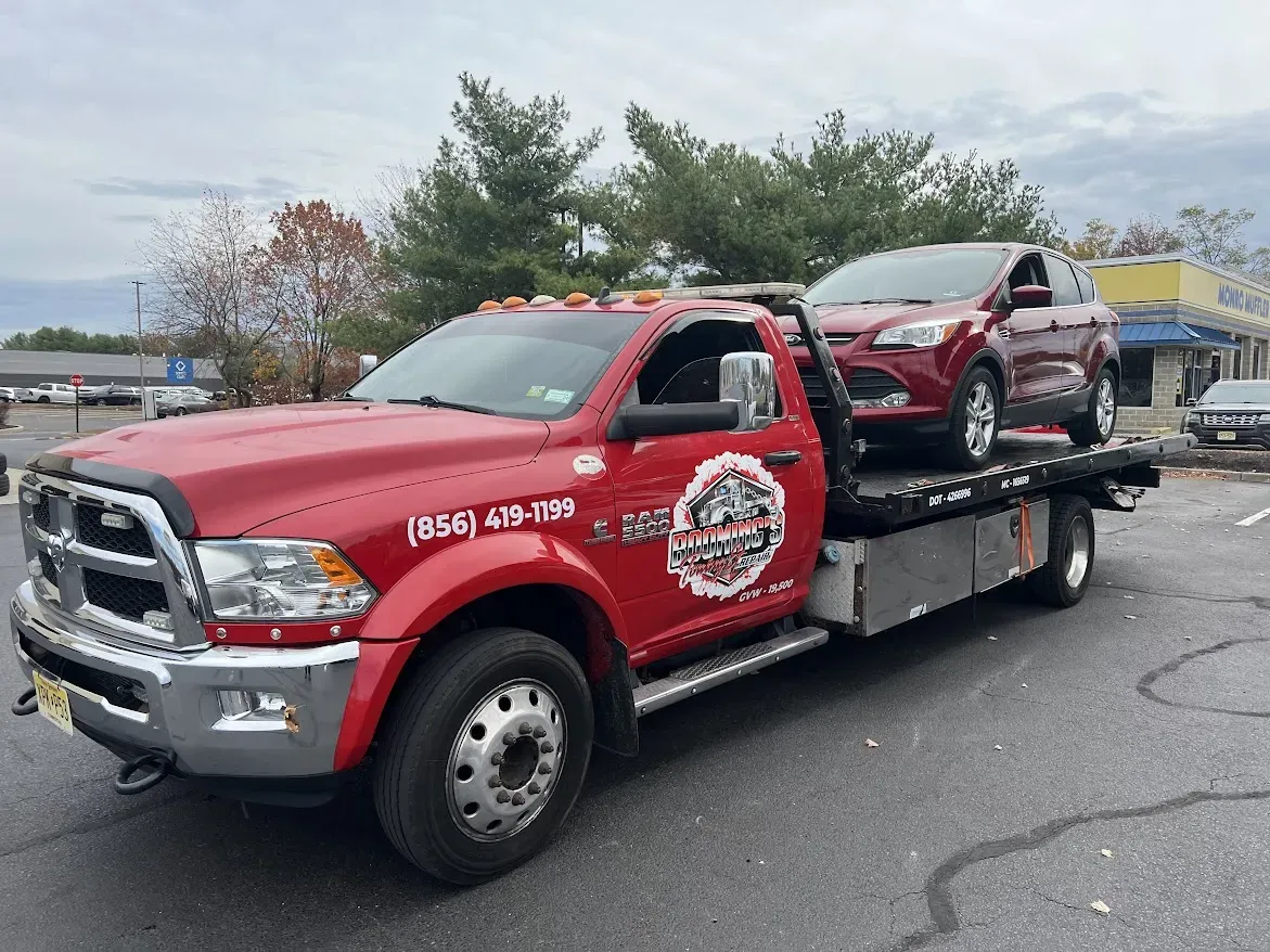 Red tow truck carrying a red car in a parking lot.