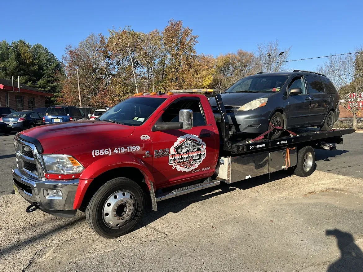 Red tow truck hauling a gray minivan on a sunny day.