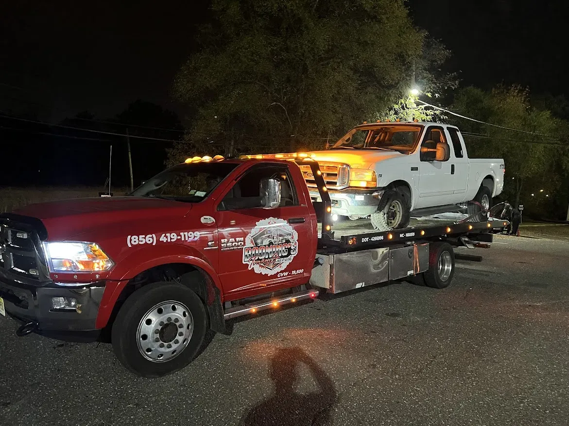 Red tow truck carrying a white pickup truck at night.