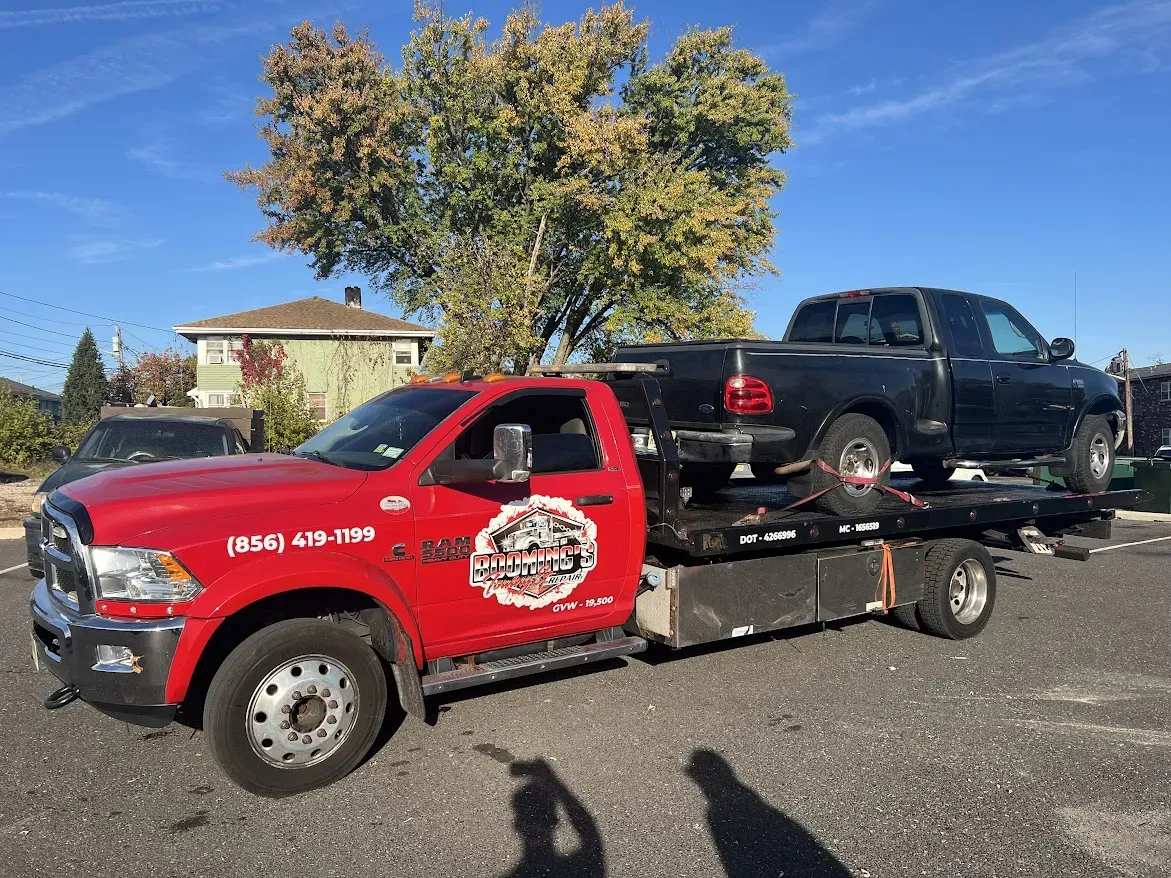 Red tow truck transporting a black pickup truck on a sunny day.