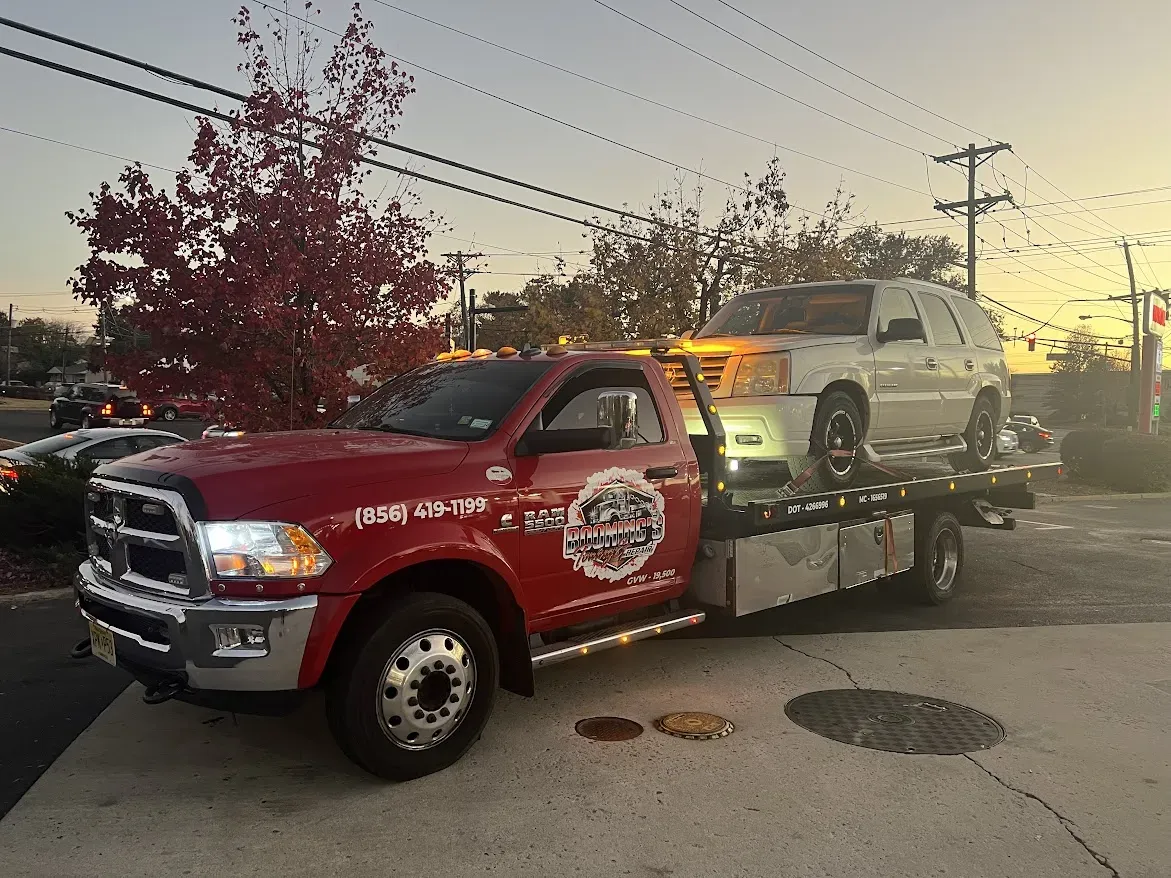 Red tow truck with a white car on its flatbed, setting sun.