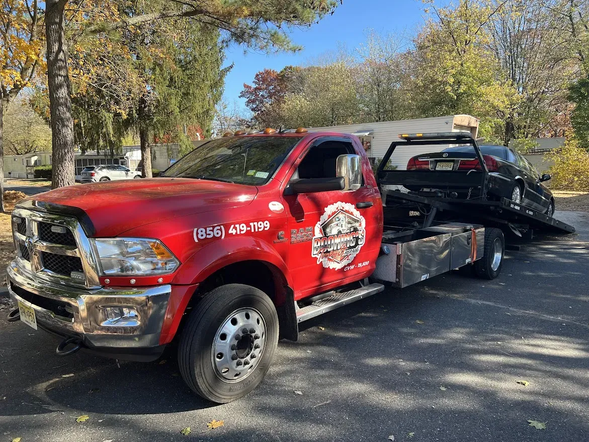 Red tow truck hauling a black car on a sunny day.