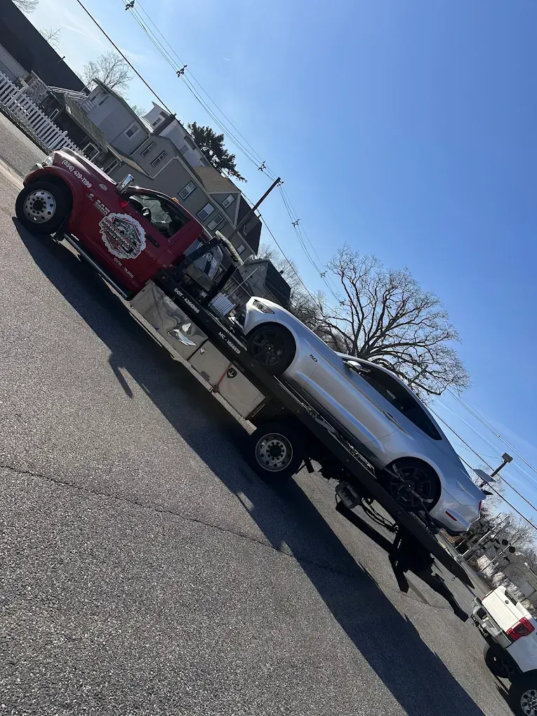 Tow truck carrying a silver car, on a sunny day.