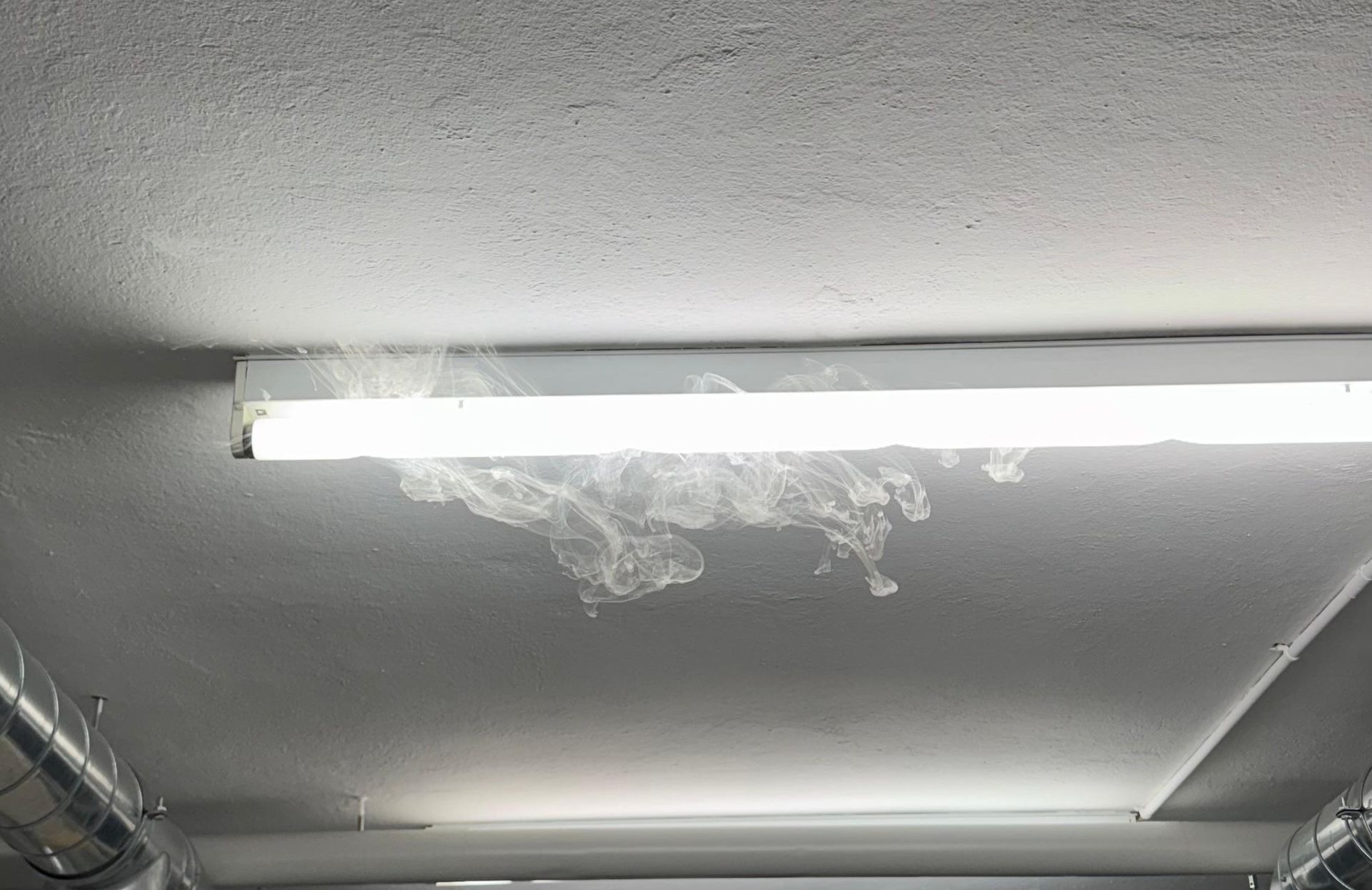 Rauch, der aus einer Leuchtstofflampe an einer weissen Decke austritt.